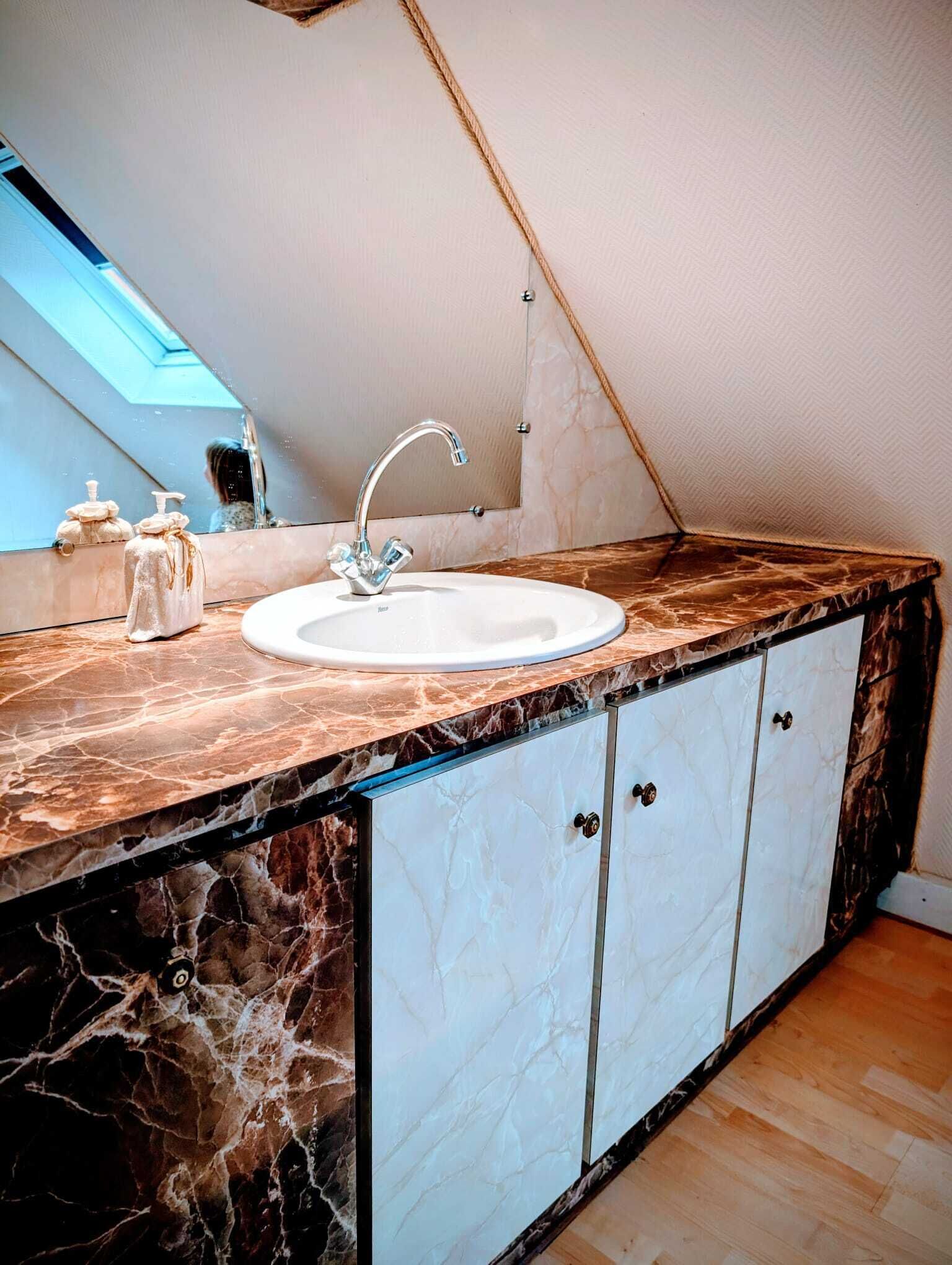 Een badkamer met een wit wastafelmeubel, een marmeren aanrechtblad en kastjes.