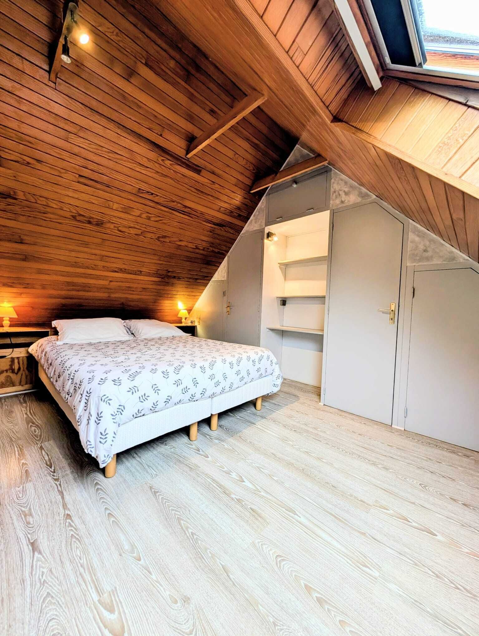 Une chambre avec un plafond en pente, un lit avec une literie à motifs, des lampes de chevet et des étagères intégrées.