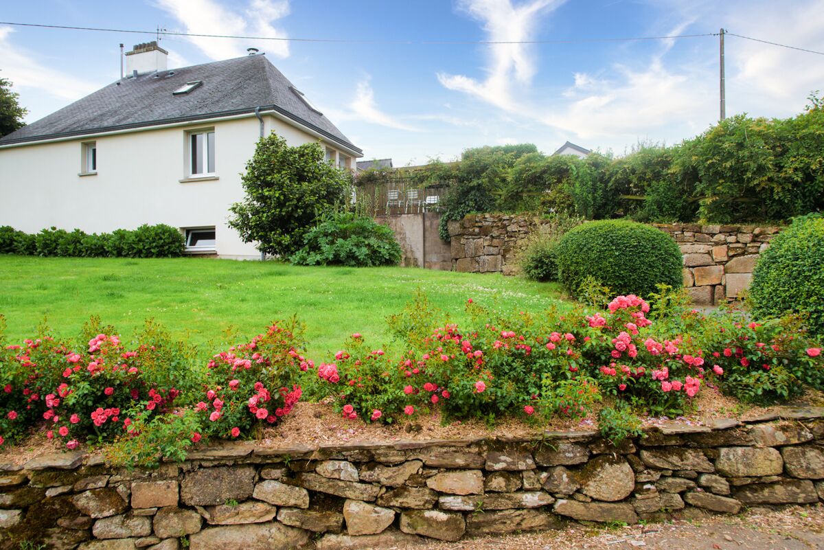 Una casa bianca con un muro in pietra e un giardino con fiori rosa.