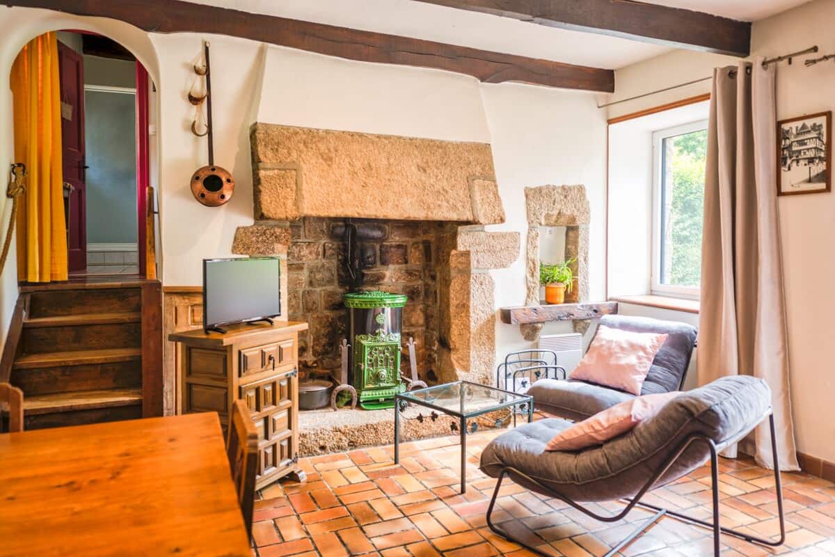 Ein gemütliches Wohnzimmer mit Kamin aus Stein, einem Fernseher auf einem Holzkabinett, einer bequemen Couch und einem Esstisch.