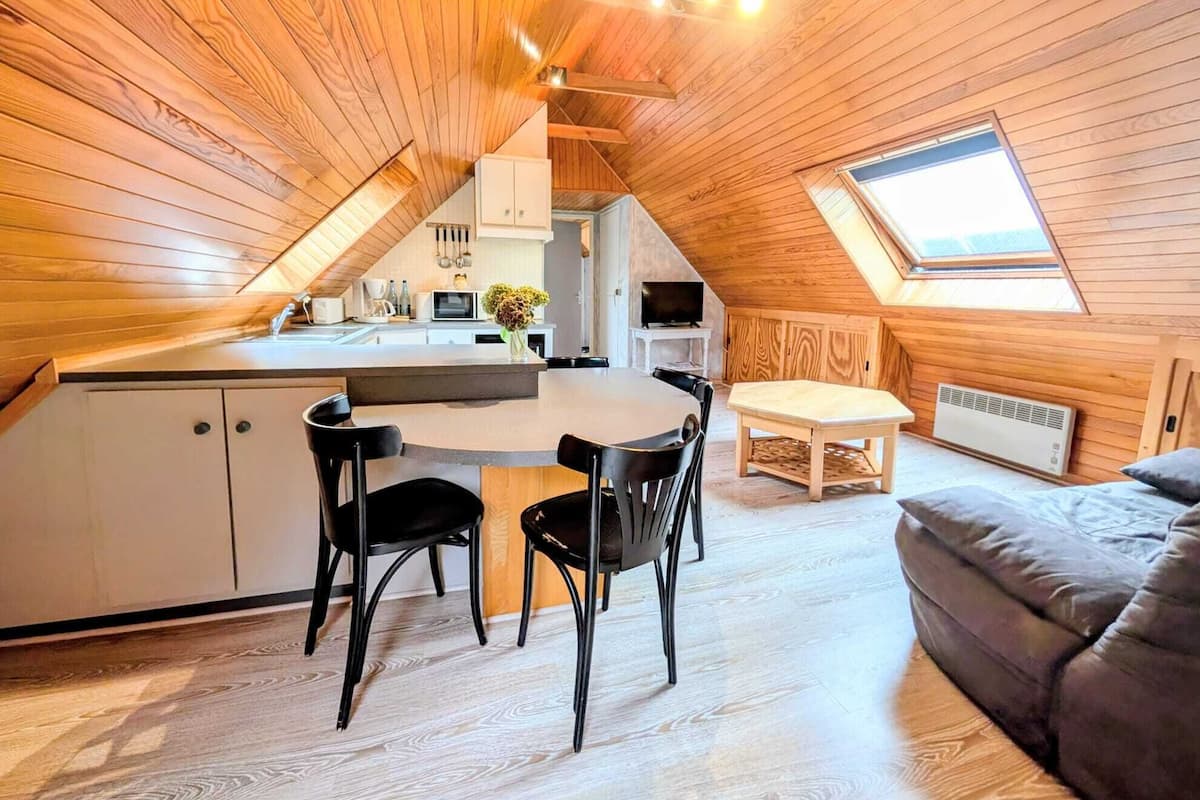 Ein gemütliches Schlafzimmer im Dachgeschoss mit Dachfenster, Holzbalkendecke, Essbereich mit Tisch und Stühlen sowie einem Bett.