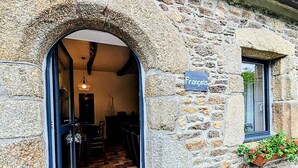 Un edificio de piedra con un arco de entrada que conduce a una habitación con piso de baldosas y una lámpara colgante.