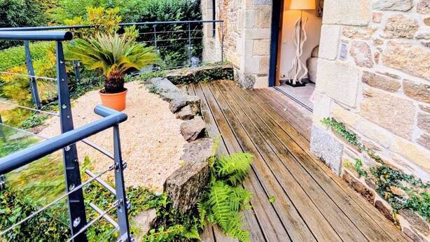 Un edificio de piedra con una terraza de madera y barandilla metálica.