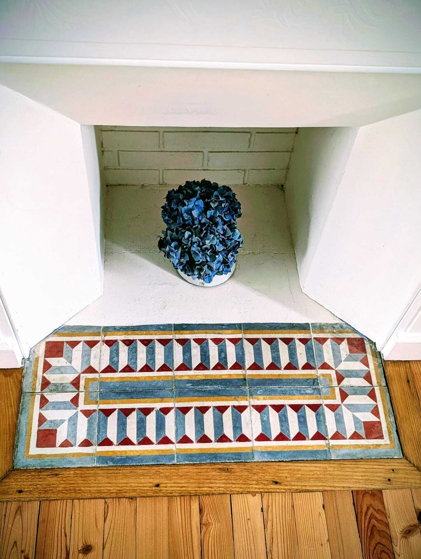 A fireplace with a blue flower arrangement and a patterned rug.