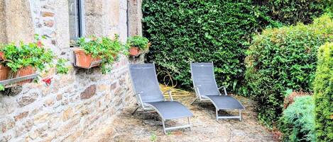 Un patio de piedra con dos sillones y plantas en macetas.