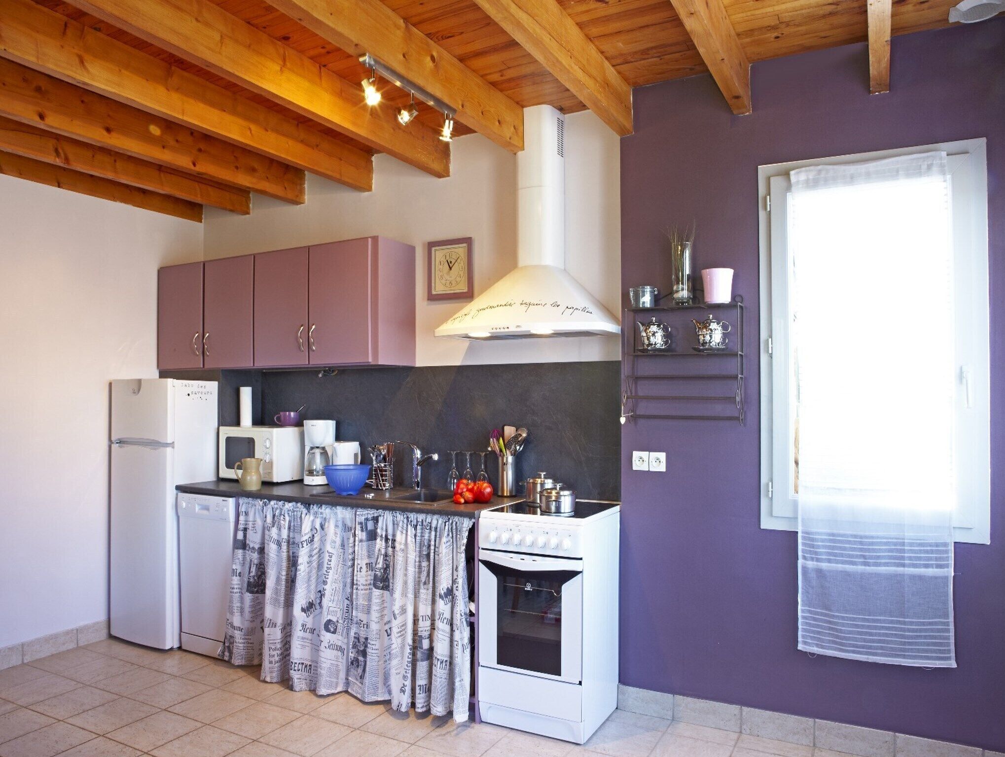 Una cocina con vigas de madera, una estufa blanca, armarios rosados y una pared morada.