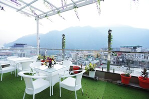 A rooftop terrace with white wicker furniture, a glass table, and potted plants. - Mystara Hotels Private Limited (Rishikesh)