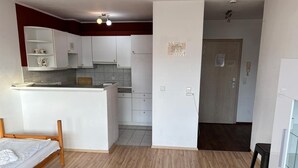 A compact room with a bed, kitchenette, and a door leading to another room.