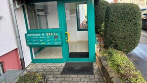 A building entrance with a green door, a sign reading "Hauptstraße 80", and a small step leading up to the entrance.