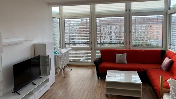 A modern living room with a large TV, a red sofa, and a white coffee table.