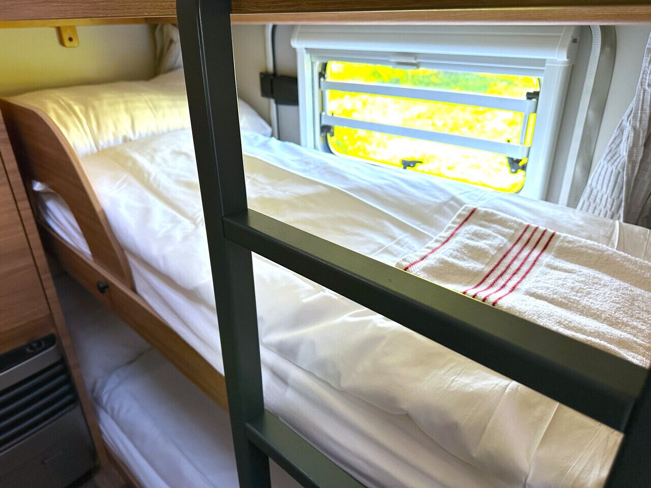 Ein Stockbett mit Fenster, einem Holzkopfstück und einer weißen Decke mit roten Streifen.