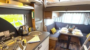 A compact RV kitchen with a sink, stove, and dining area.