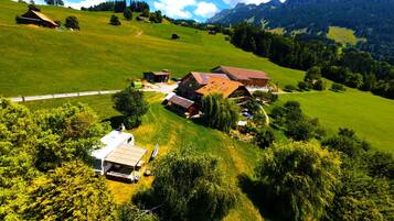 Paesaggio rurale con una casa colonica, una piccola stalla e un camper bianco parcheggiato su una collina erbosa.