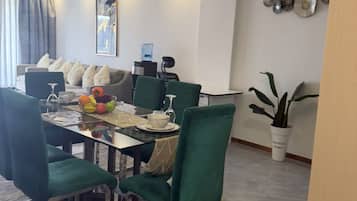 Un comedor con una mesa dispuesta para cuatro, sillas tapizadas en verde, un tapete estampado y un adorno en la pared.