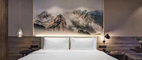 Una habitación de hotel moderna con una cama grande, una mesita de noche con lámpara, un teléfono en la pared y un cuadro decorativo de montañas.