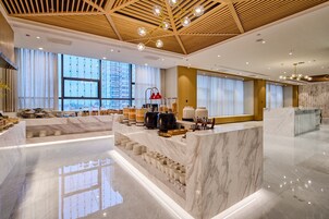 Un moderno vestíbulo de hotel con un mostrador de recepción de mármol, ventanas amplias y techo de madera.