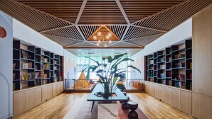 Interior de una biblioteca moderna con suelos de madera, estanterías, una mesa central con una planta y un diseño geométrico en el techo.