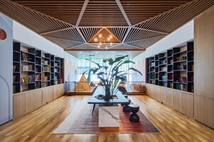 Interior de una biblioteca moderna con suelos de madera, estanterías, una mesa central con una planta y un diseño geométrico en el techo.