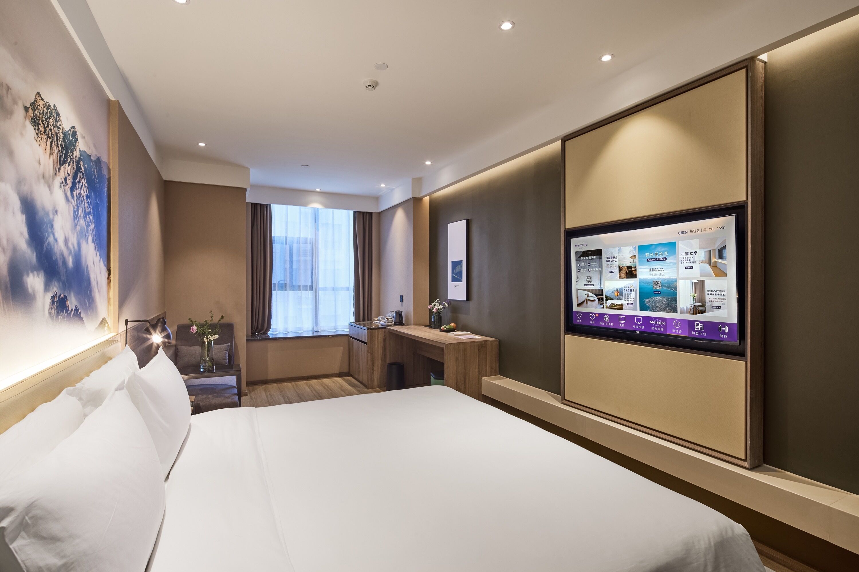 A modern hotel room with a large bed, a desk, a TV, and a wall-mounted control panel.