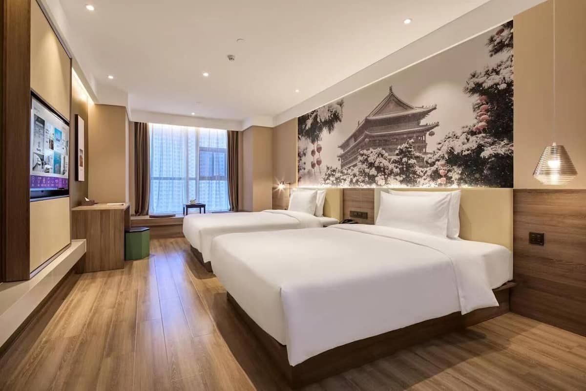 A hotel room with two beds, a large window, and a traditional-style mural on the wall.
