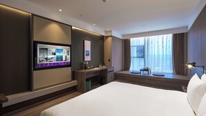 Una habitación de hotel moderna con una cama grande, un escritorio, un televisor y una ventana con cortinas.