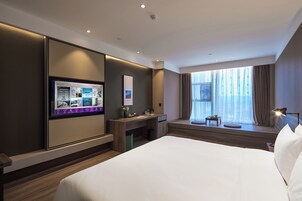 Una habitación de hotel moderna con una cama grande, un escritorio, un televisor y una ventana con cortinas.
