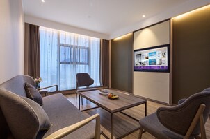 Una habitación de hotel moderna con un ventanal grande, una mesa de centro de madera y una zona de estar con dos sofás y una silla.