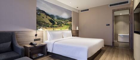 A modern hotel room with a large bed, a desk with a lamp, a chair, and a scenic mural on the wall.