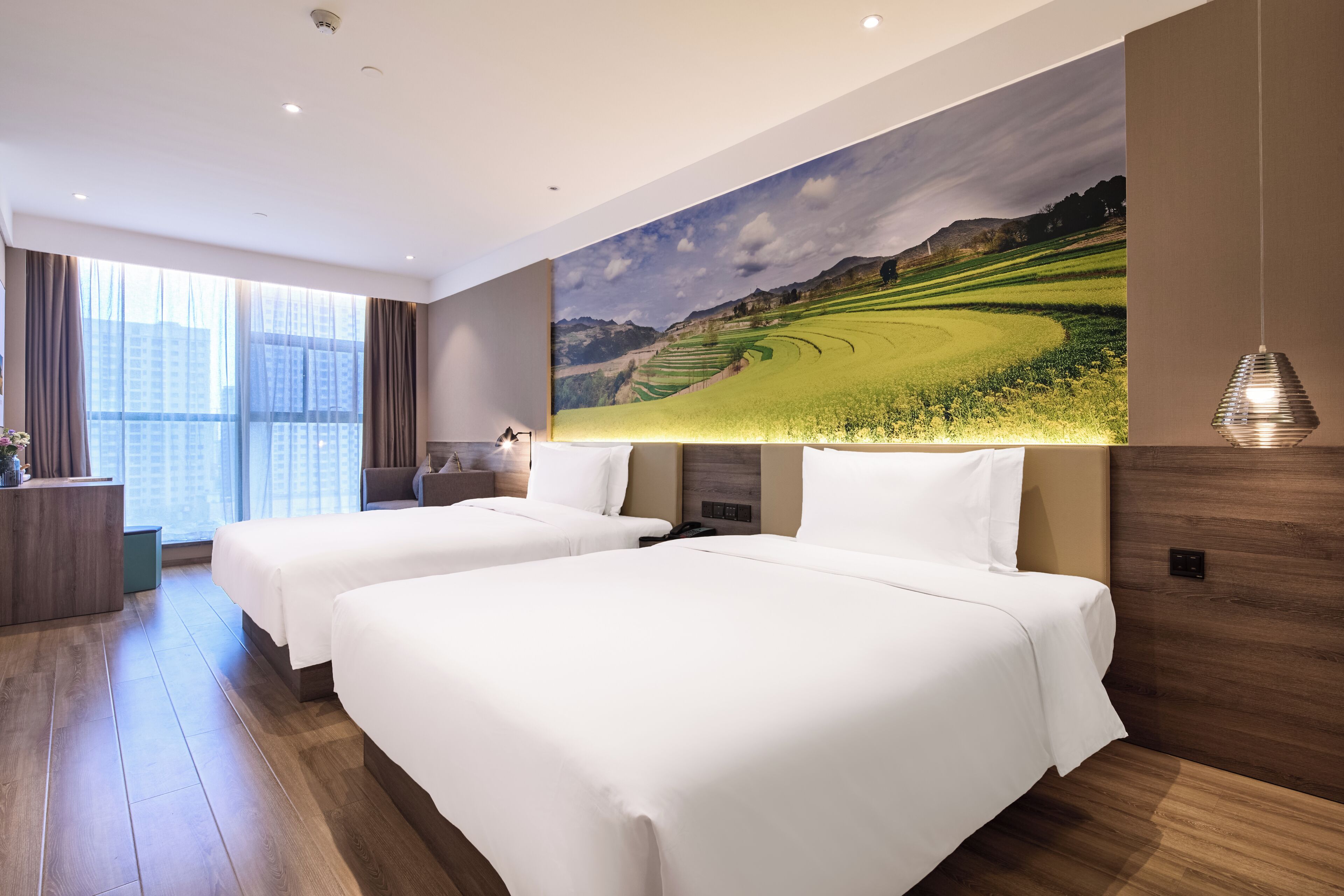Een hotelkamer met twee bedden, een bureau, een stoel, een groot raam en een aan de muur hangend schilderij.