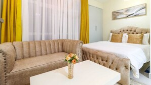 Ein Hotelzimmer mit einer Couch, einem Bett, einem weißen Tisch und einer Vase mit Blumen.