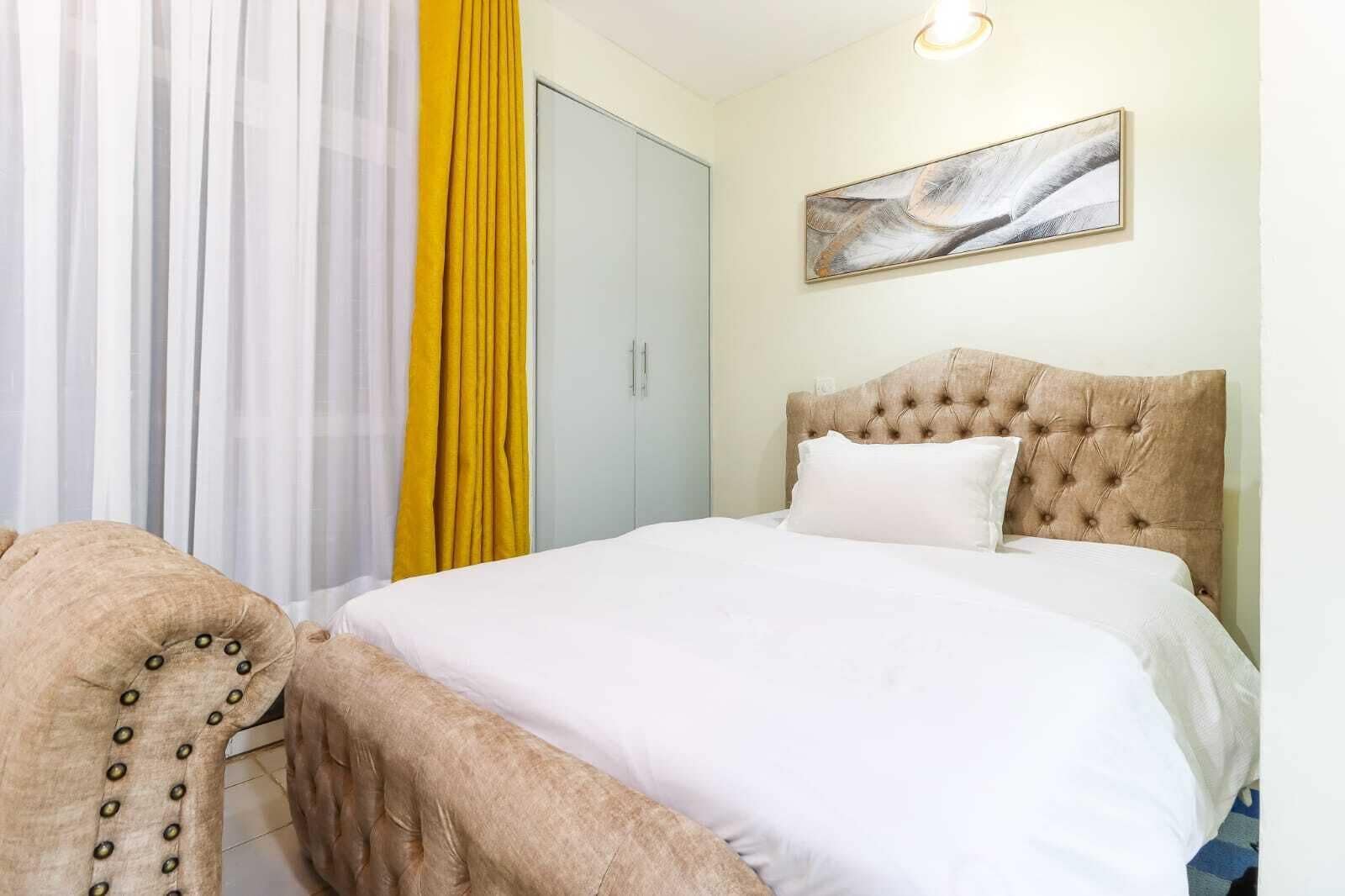 A bedroom with a bed, a wardrobe, a chair, and a painting on the wall.