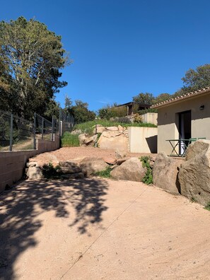 Un'area esterna recintata con un edificio, rocce grandi e alberi.
