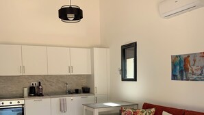 A modern kitchen with white cabinets, a gas stove, and a hanging light fixture. - Mini Villa, 15mn from Porto Vecchio (Sotta)