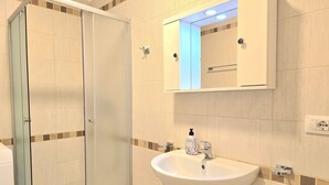 Ein Badezimmer mit Duschkabine aus Glas, einem weißen Waschbecken mit Spiegel darüber und einer kleinen Toilette.
