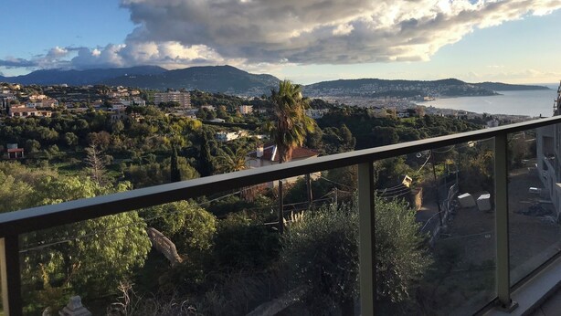 A balcony with a view of a coastal town, buildings, and mountains in the distance. - Blue Pearl A102 by Avecoeur (Nice)