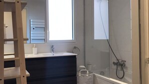 A modern bathroom with a glass shower enclosure, a dark vanity, and a window providing natural light. - Blue Pearl A102 by Avecoeur (Nice)