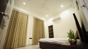 Habitación de hotel con cama, cortinas, unidad de aire acondicionado, televisor y una planta.
