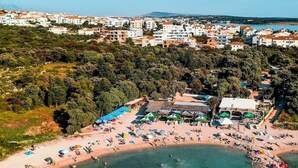 An aerial view of a coastal town with a beach area featuring umbrellas and people.