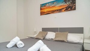 A neatly made bed with white and beige pillows, a gray bedspread, and rolled white towels on the bed.