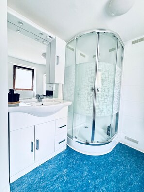 A modern bathroom with a curved glass shower enclosure, white cabinets, and a blue marble floor. - Comfortable 2BR Apt for 7 Guests (Vienna)