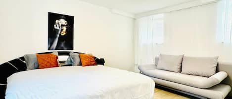 A modern bedroom with a large bed, a sofa, and a poster on the wall.