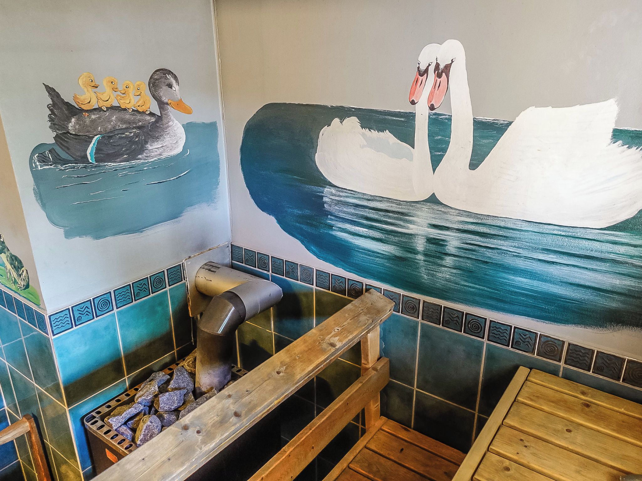 Un bagno con un murale raffigurante anatre e cigni, una panca in legno e una parete piastrellata.