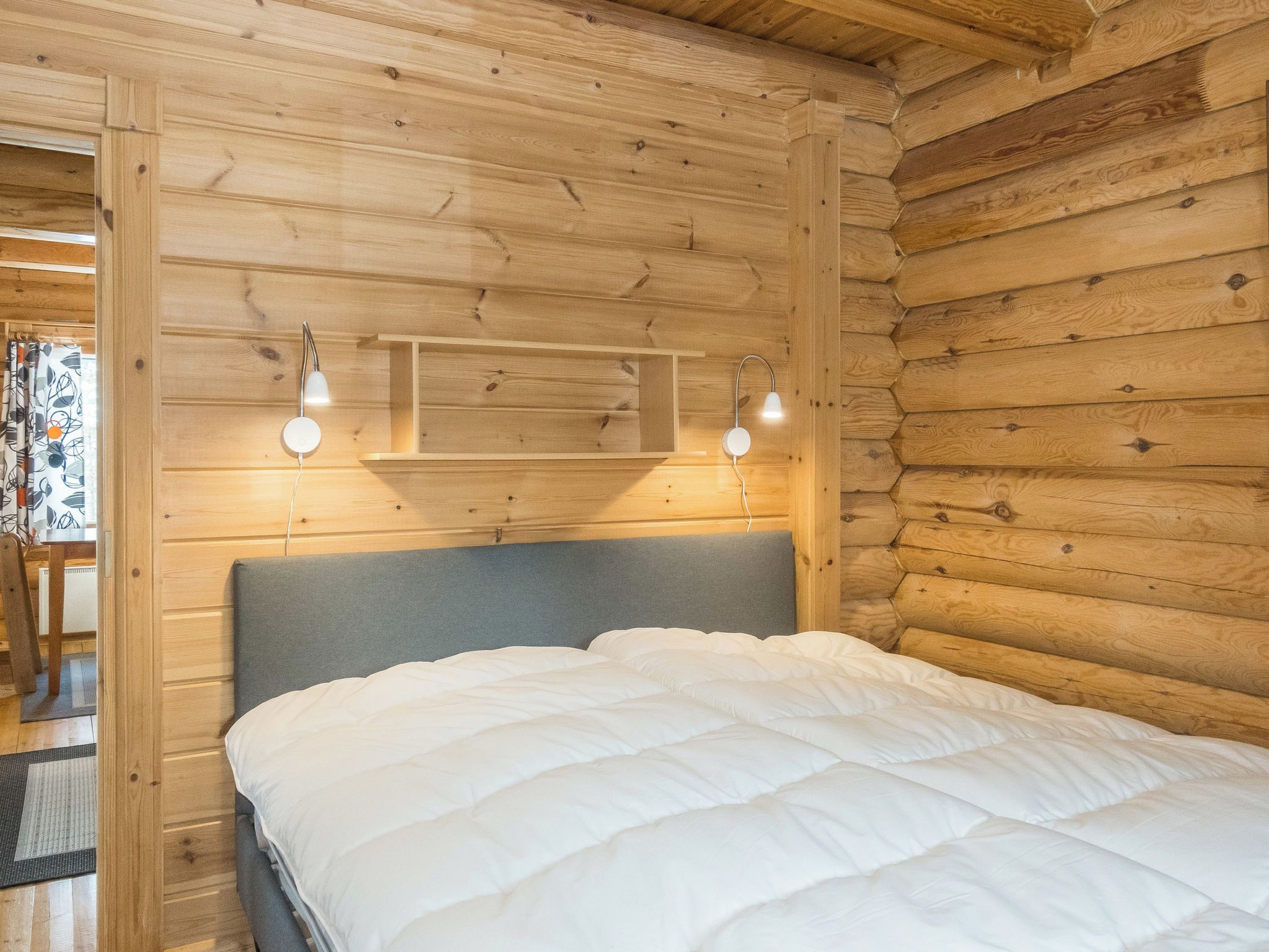 A wooden cabin room with a bed, two wall-mounted lights, and a built-in shelf.