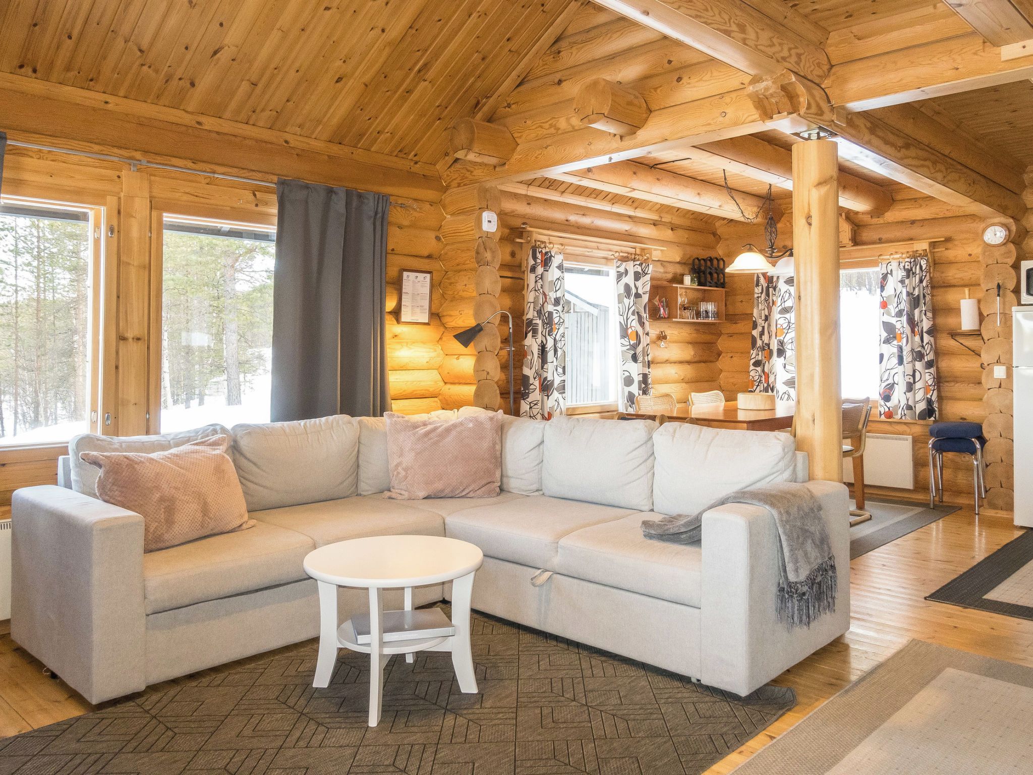 A log cabin interior with a sectional sofa, a small round table, and a dining area with a wooden table and chairs.