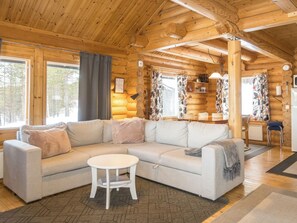 A log cabin interior with a sectional sofa, a small round table, and a dining area with a wooden table and chairs. - Kultaranta ii by Interhome (Inari)