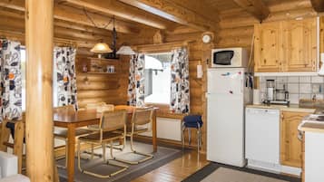 A wooden cabin interior with a dining area, kitchen, and a window with curtains.