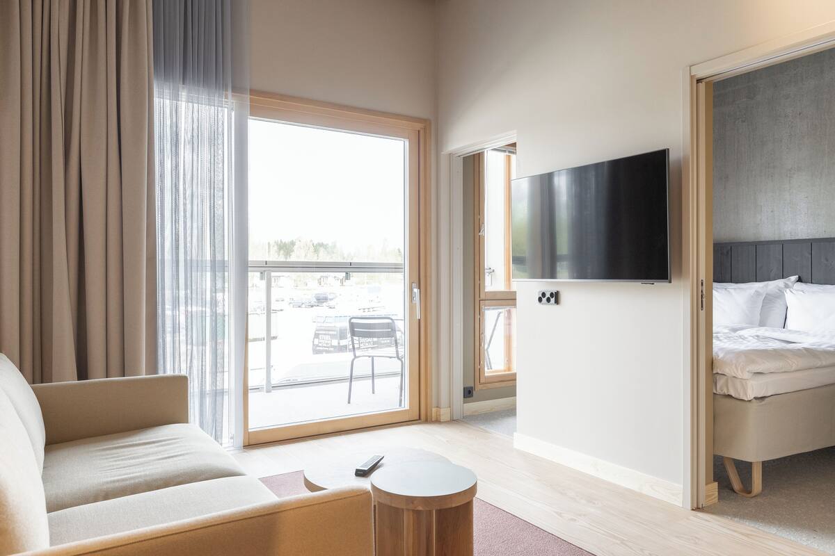 A hotel room with a sofa, a TV mounted on the wall, a bed, and a small round table.