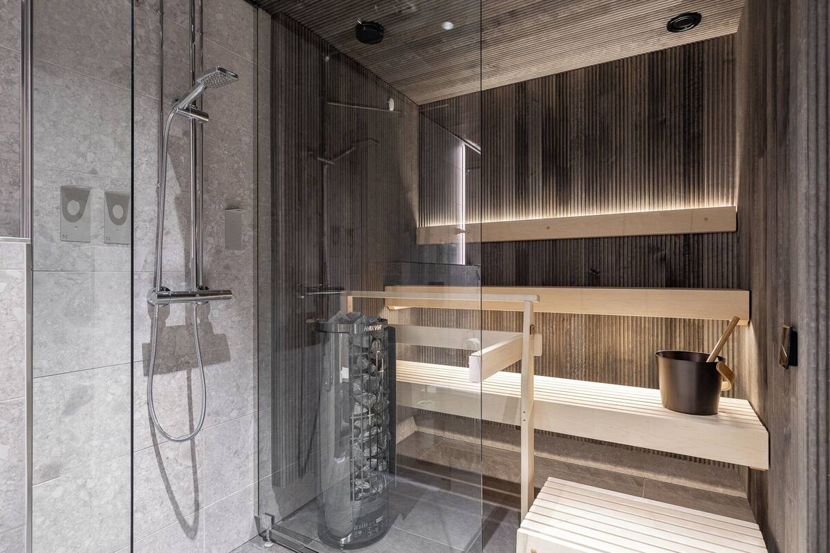 A modern shower area with a glass enclosure, a built-in bench, and a metal bucket.