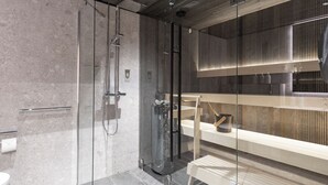 A modern bathroom with a glass shower enclosure, a wooden bench, and a large mirror. - Break Sokos Hotel Himos (Jamsa)