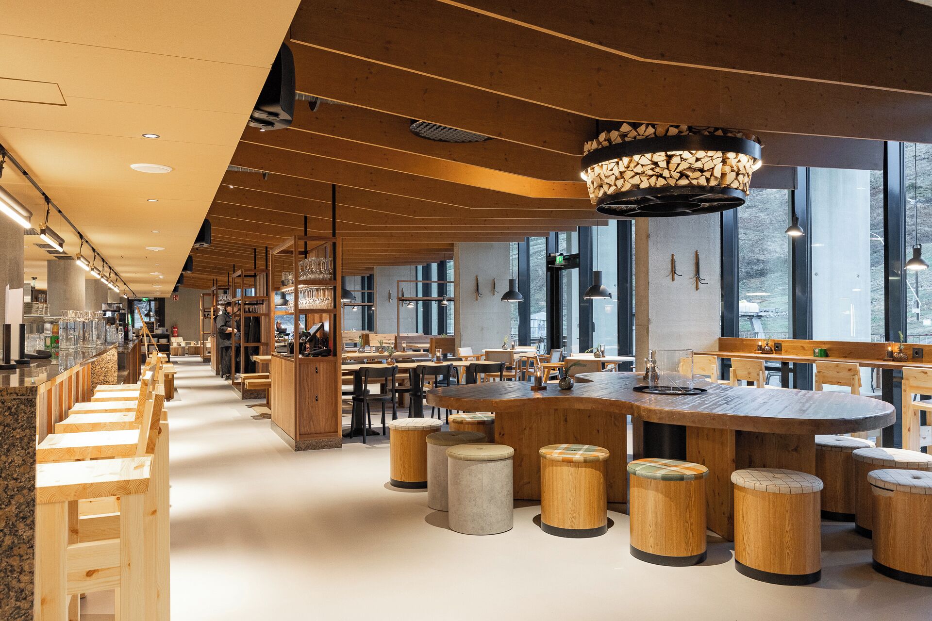 Un interior de restaurante moderno con mobiliario de madera, ventanas amplias y una zona de bar central.